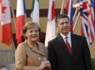 Bundeskanzlerin Merkel und Professor Sauer warten vor Fahnen auf ihre Gäste
