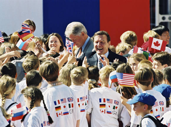 Bundeskanzler Gerhard Schröder und der amerikanische Präsident Bill Clinton werden von Kindern mit Fahnen begrüßt.